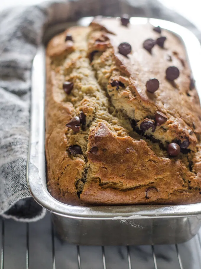 Sourdough banana bread in loaf pan on a cooling rack on a marble surface.