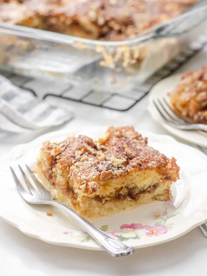 A slice of sourdough coffee cake on a small plate with a fork to the side with the pan in the background on a wire cooling rack.