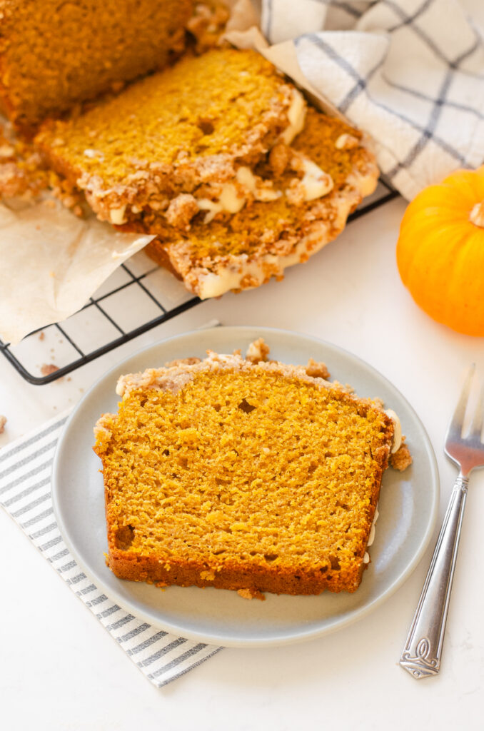 A slice of sourdough pumpkin bread on a plate with the loaf in the background.