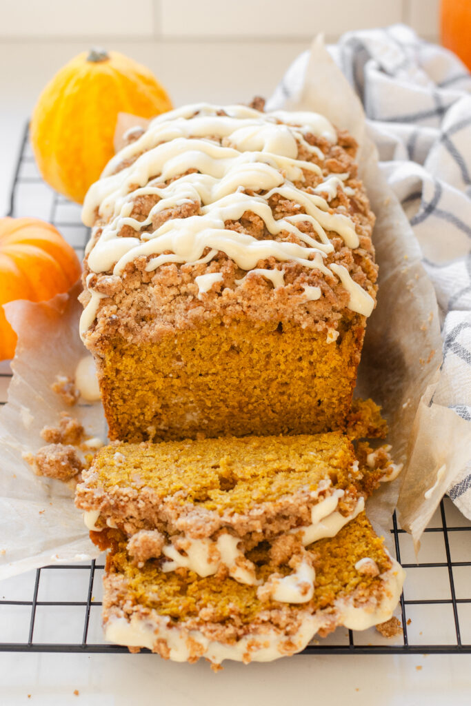 A loaf of sourdough pumpkin bread on a wire cooling rack with tiny pumpkins and a tea towel off to the side.