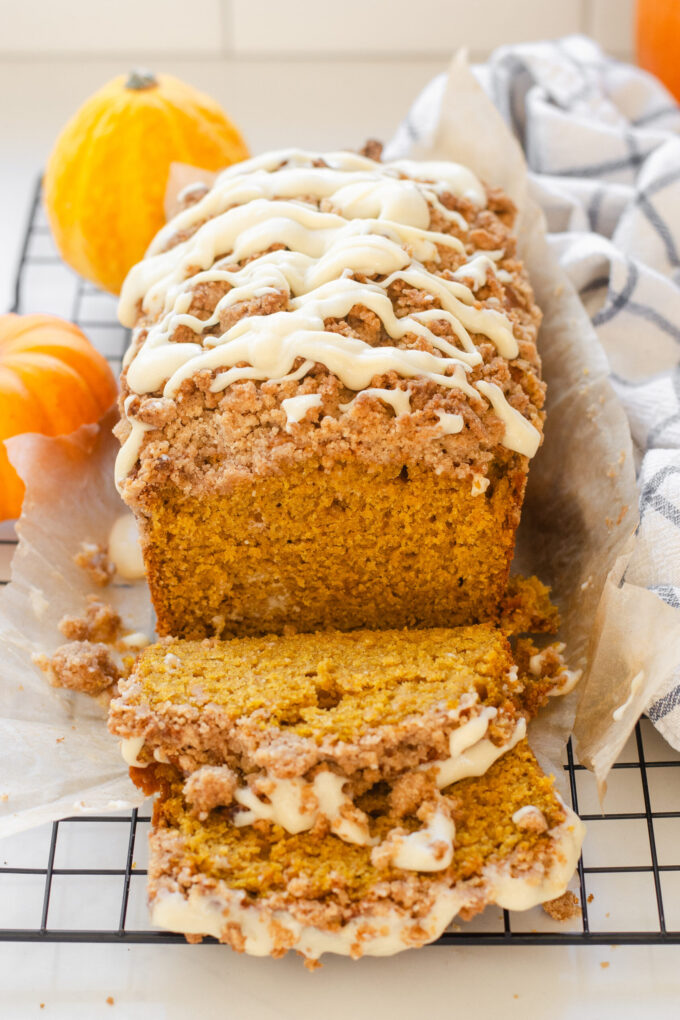 A loaf of sourdough pumpkin bread on a wire cooling rack with tiny pumpkins and a tea towel off to the side.