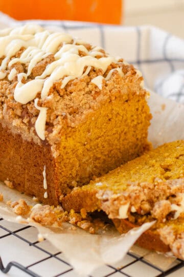 A loaf of sourdough pumpkin bread on a wire rack with a few pieces cut.