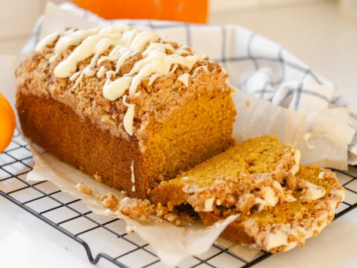 A loaf of sourdough pumpkin bread on a wire rack with a few pieces cut.