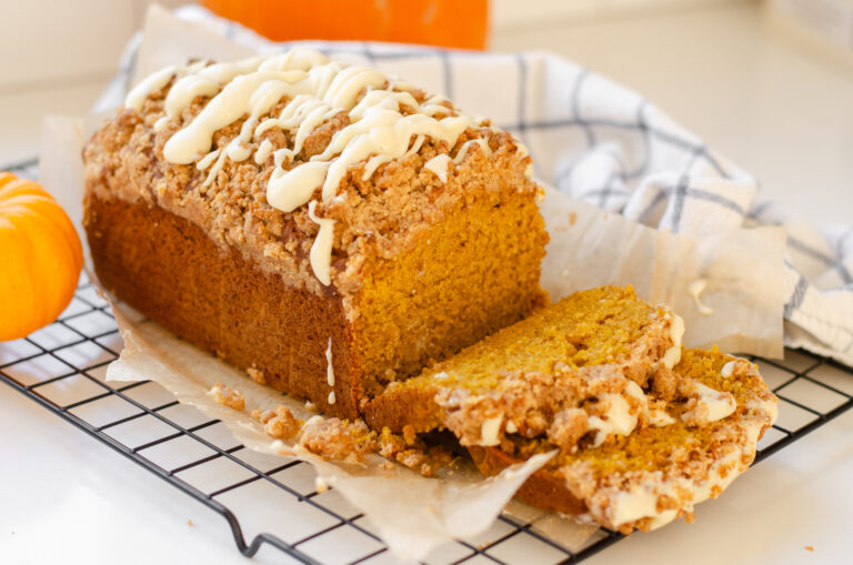 A loaf of sourdough pumpkin bread on a wire rack with a few pieces cut.