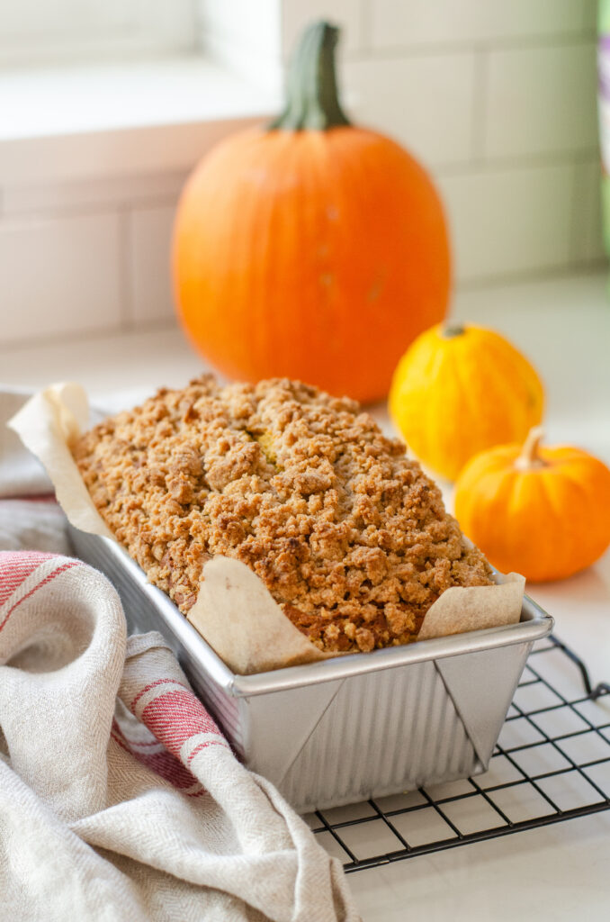 A loaf of sourdough pumpkin bread cooling in a pan on a wire rack.