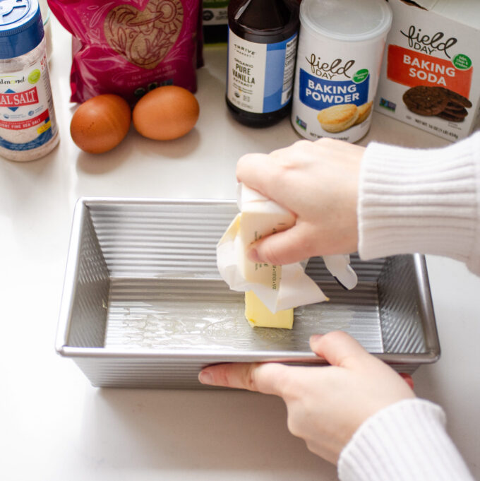 Greasing a pan by rubbing it with a stick of butter.
