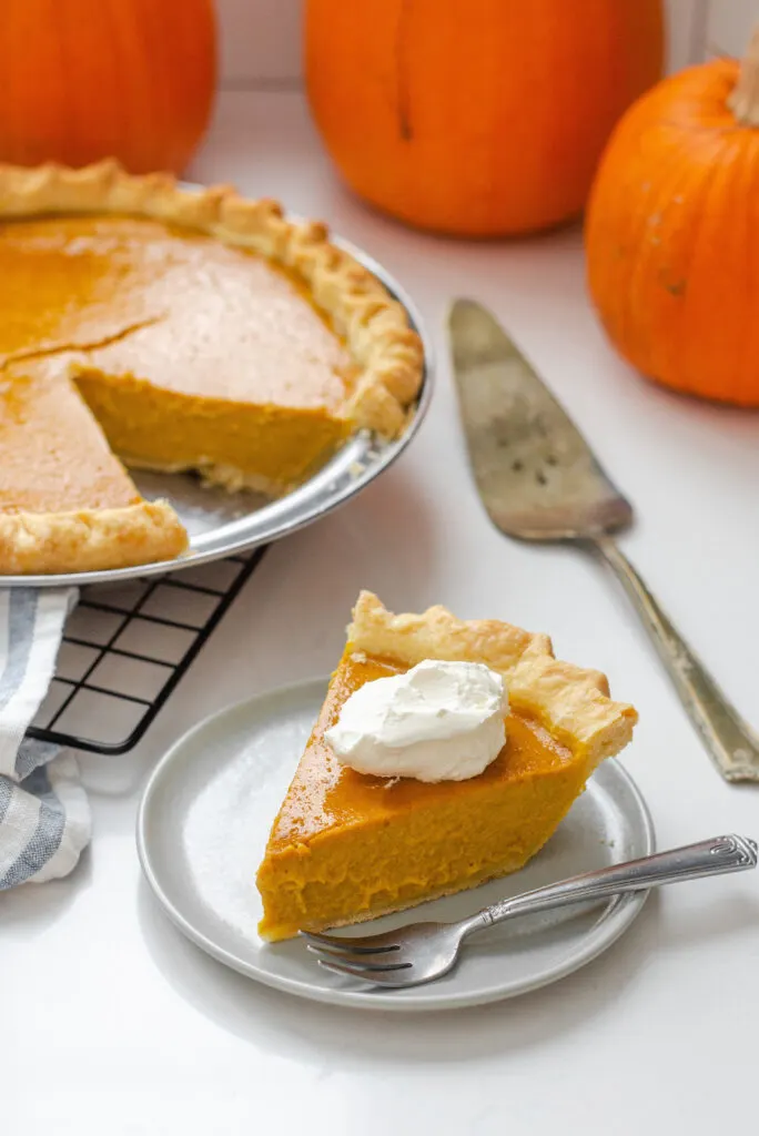 A piece of low sugar pumpkin pie on a plate with the rest of the pie in the background on a wire cooling rack.