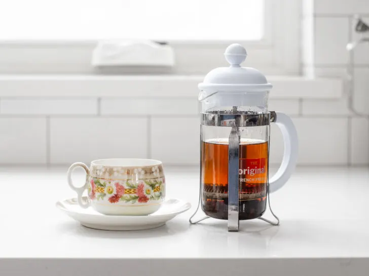 A teacup with a French press filled with black tea next to it.