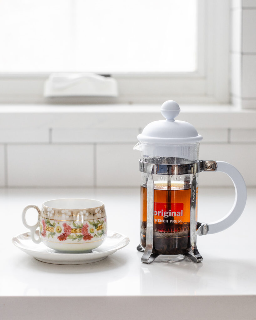 A teacup with a French press filled with black tea next to it.