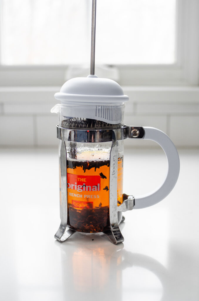 A French press on a white countertop with black tea steeping inside it.
