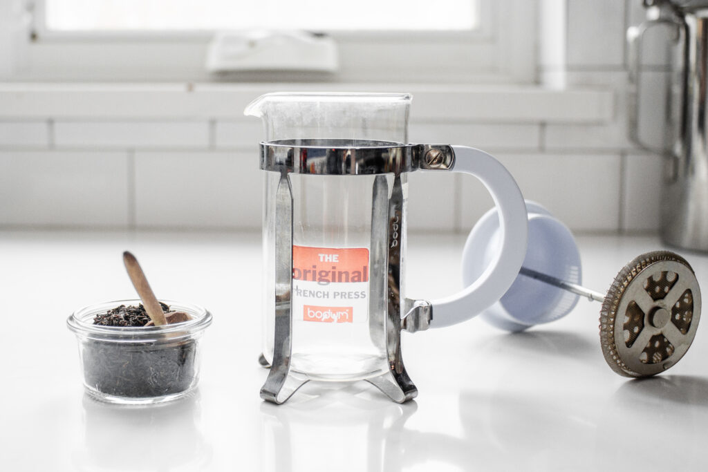 A French press with a jar of loose leaf tea next to it.