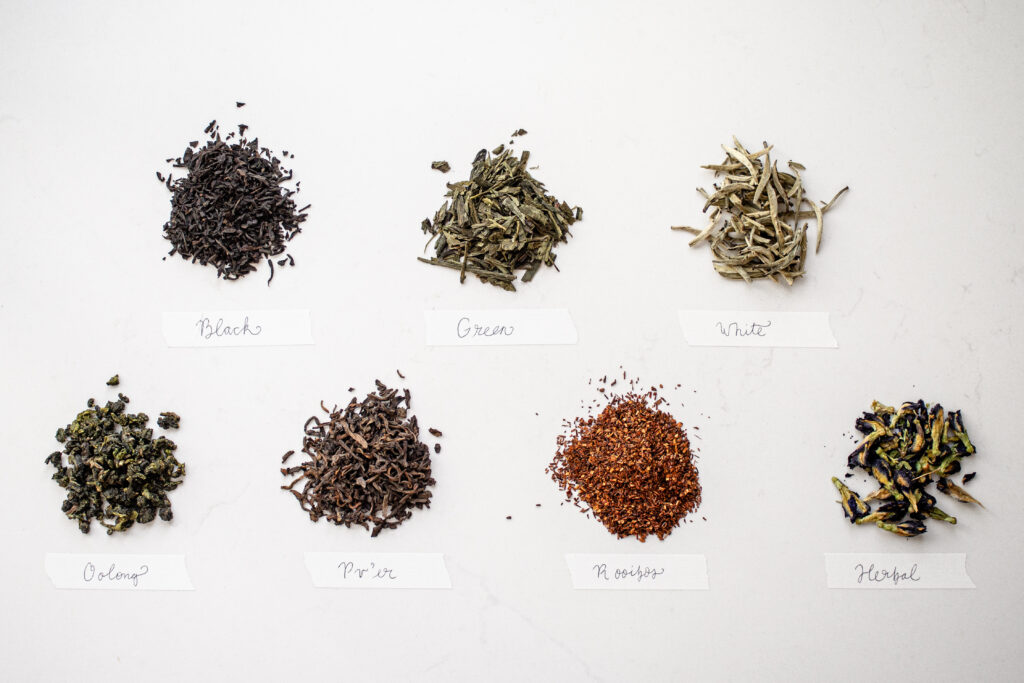 Different types of tea laid out on a white countertop with labels.