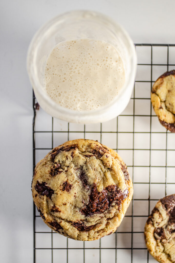 A stack of chocolate chip sourdough cookies with a jar of sourdough starter discard to the side.