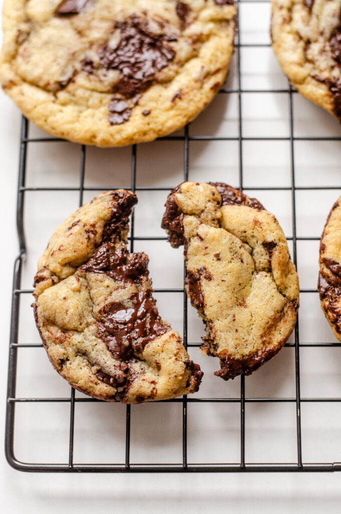 A broken sourdough chocolate chip cookie on a wire cooling rack with other cookies around it.