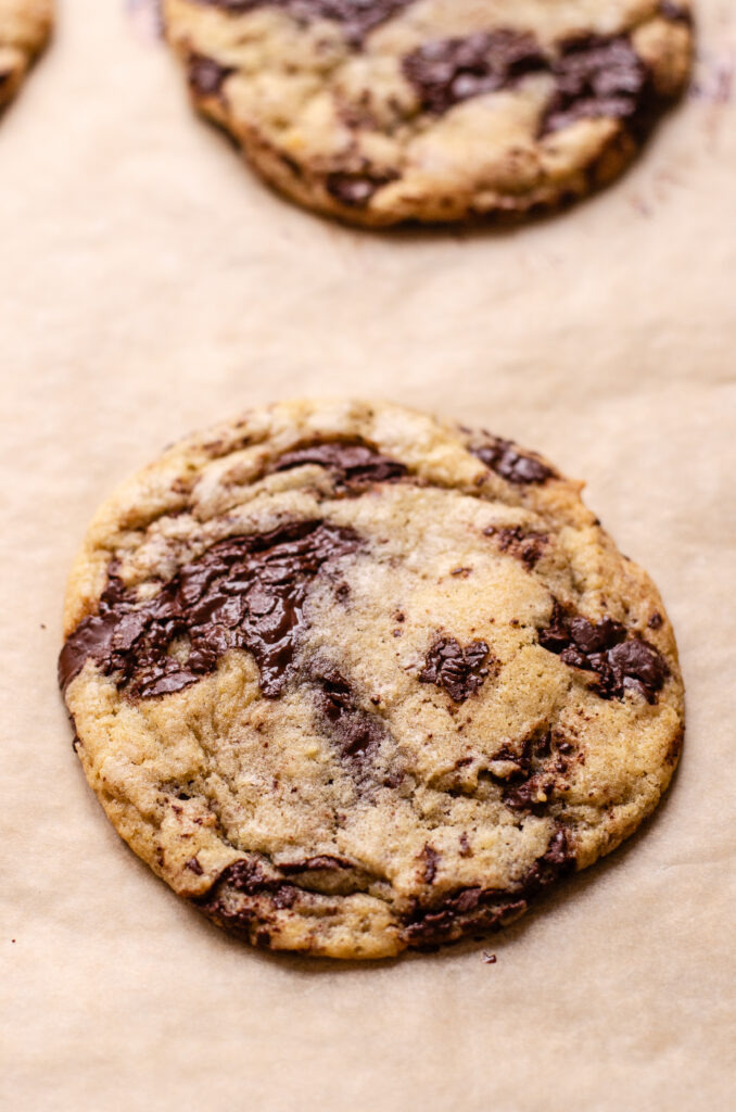 A baked chocolate chip sourdough cookie on a baking sheet lined with parchment paper.