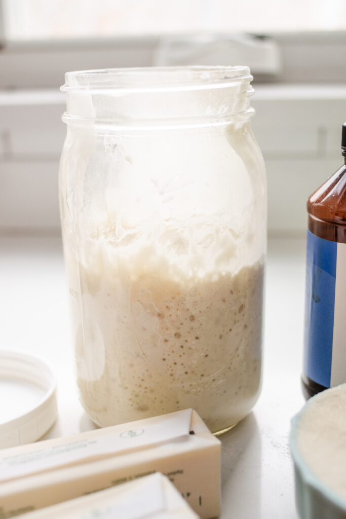 A jar of sourdough starter on a kitchen counter with other ingredients around it.
