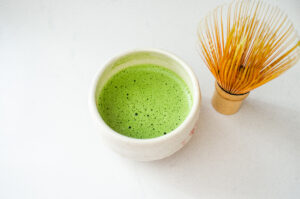 A stone bowl with frothy matcha and a bamboo whisk off to the side.