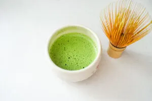 A stone bowl with frothy matcha and a bamboo whisk off to the side.