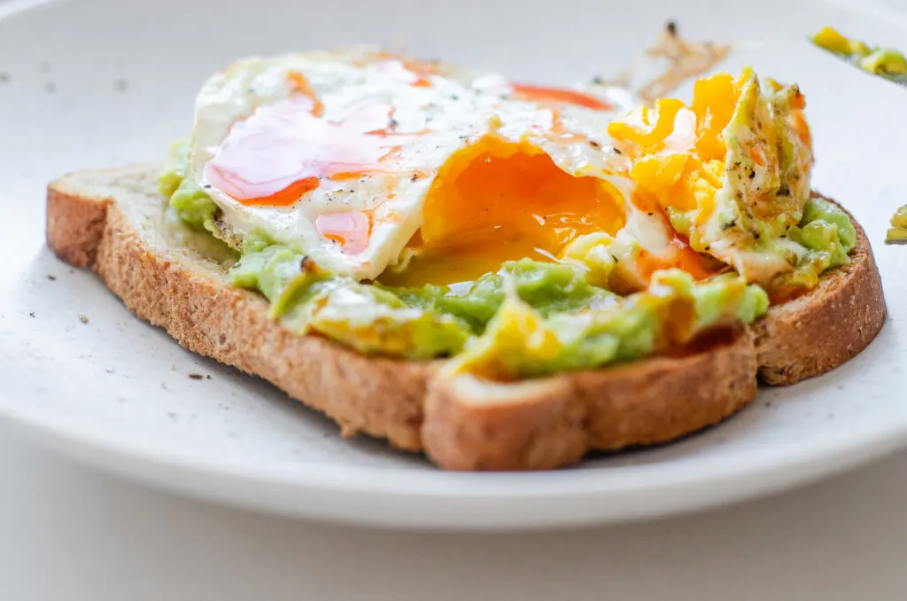 A fried egg (over medium) on avocado toast cut open so show the yolk.