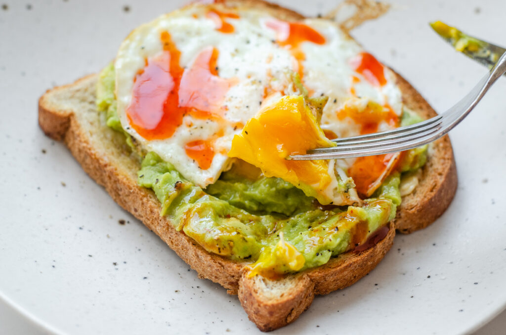 A fried egg (over medium) on avocado toast with a piece of the yolk on a fork.