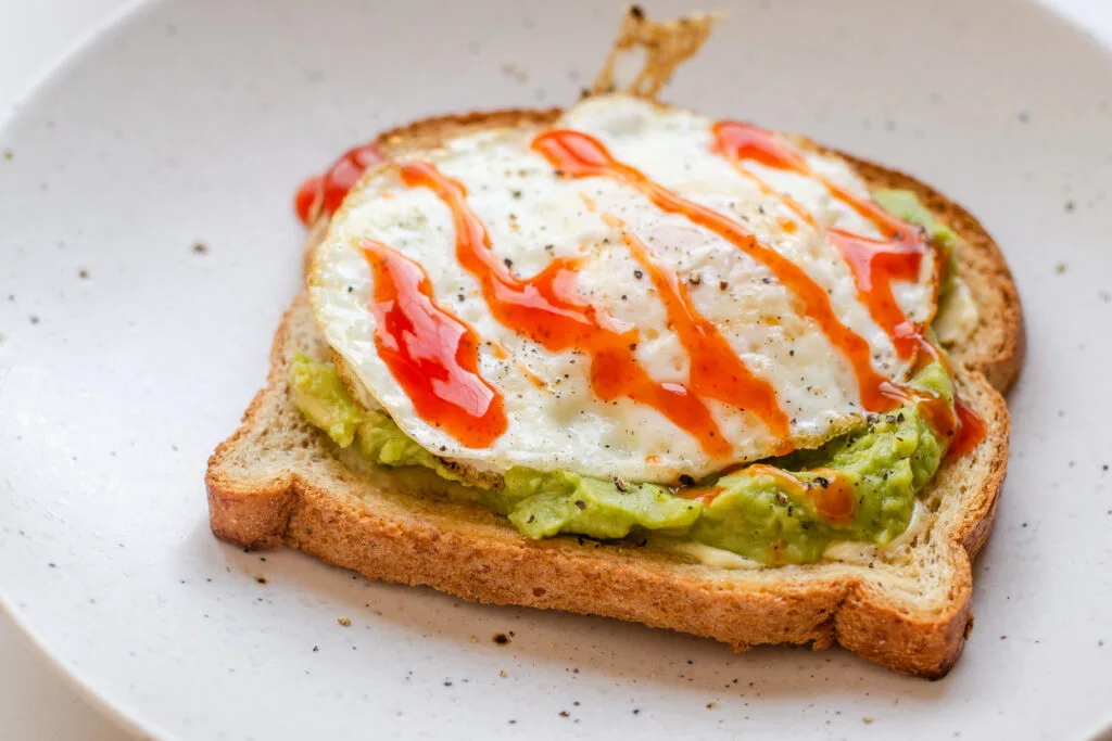 A fried egg (over medium) on avocado toast with hot sauce drizzled on top.