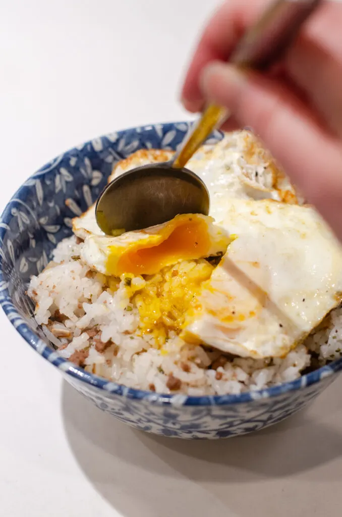 Cutting into a fried egg on top of a rice bowl.