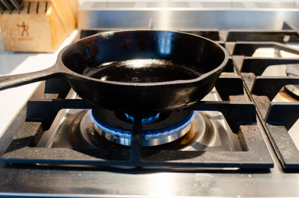 A small cast iron skillet on a stovetop with the heat set to medium-low.