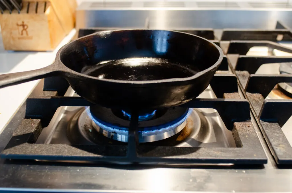 A small cast iron skillet on a stovetop with the heat set to medium-low.