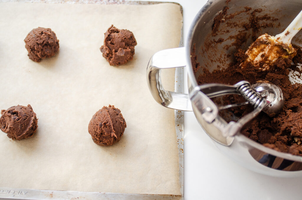 Placing balls of cookie dough on a parchment lined baking sheet.