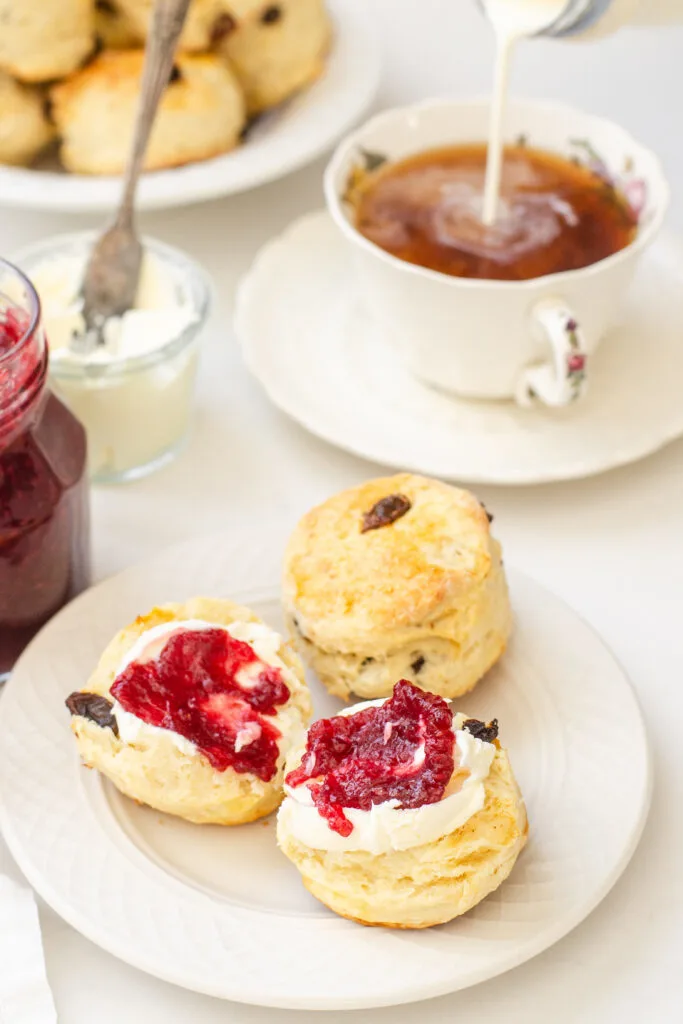 Irish Scones made with buttermilk on a small plate with a teacup, jam, and Devonshire cream in the background.