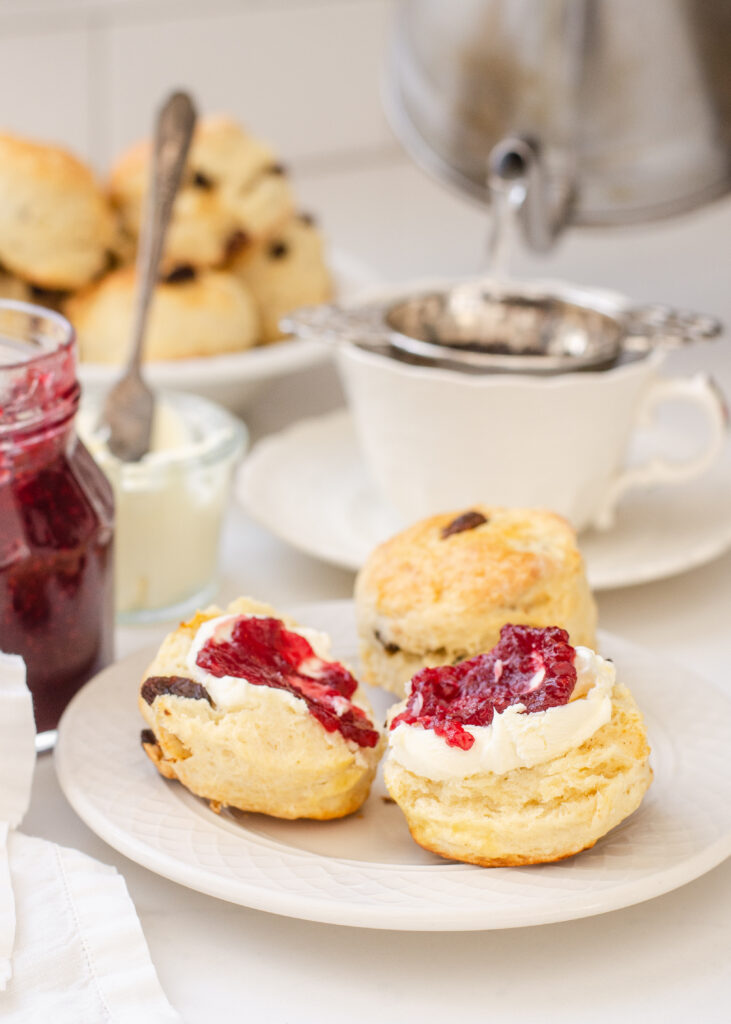 Irish Scones made with buttermilk on a small plate with a teacup, jam, and Devonshire cream in the background.