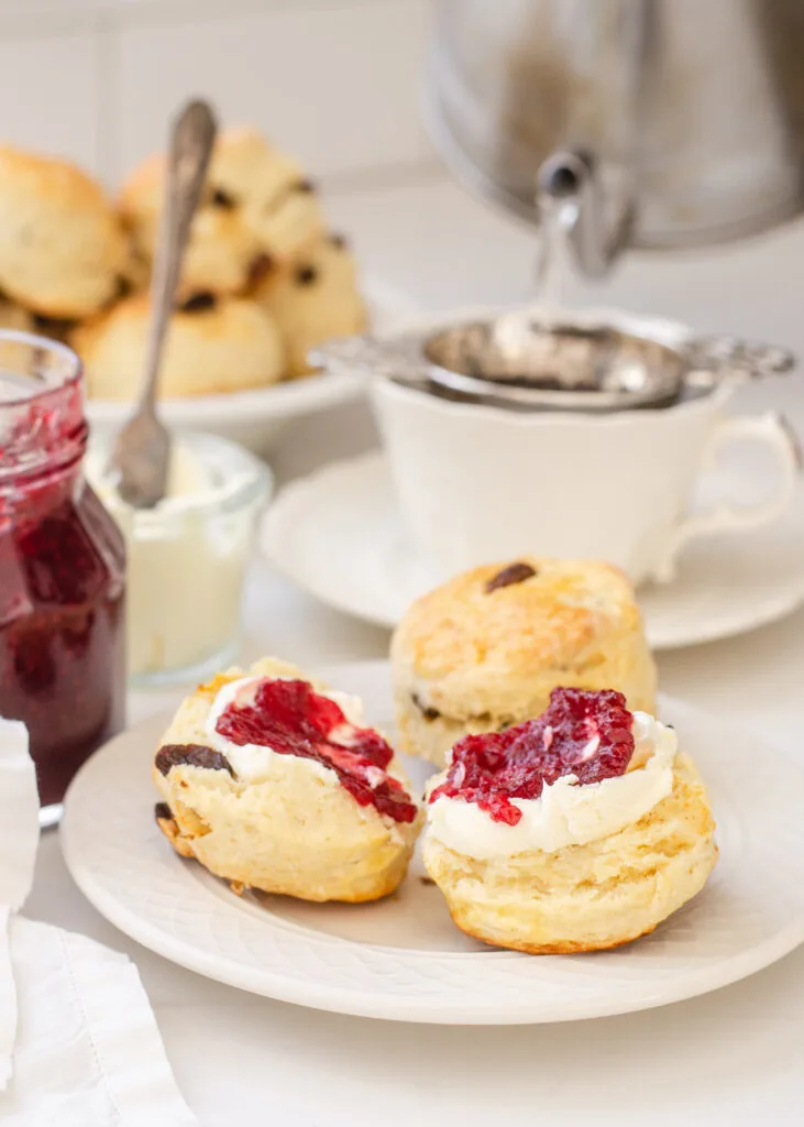 Irish Scones made with buttermilk on a small plate with a teacup, jam, and Devonshire cream in the background.