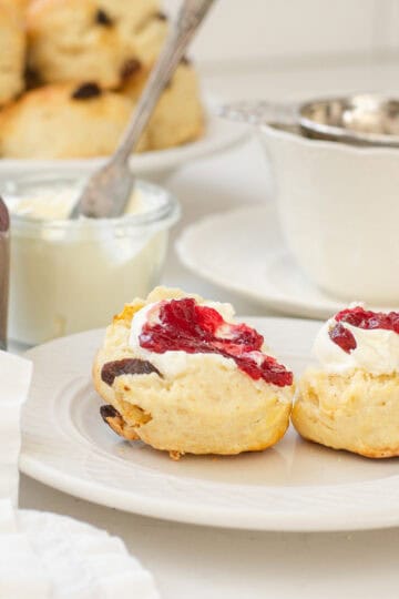Irish Scones made with buttermilk on a small plate with a teacup, jam, and Devonshire cream in the background.