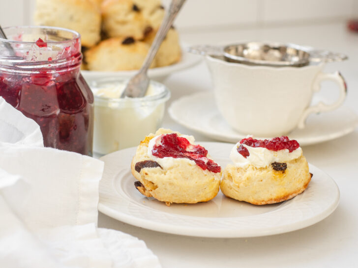 Irish Scones made with buttermilk on a small plate with a teacup, jam, and Devonshire cream in the background.