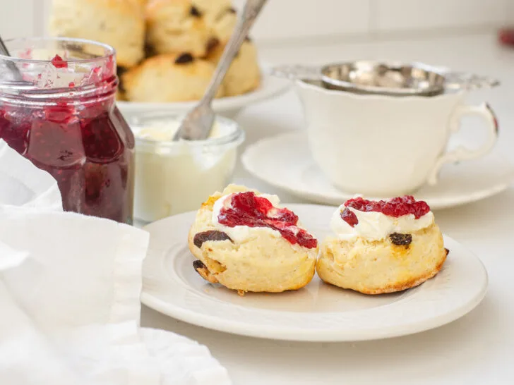 Irish Scones made with buttermilk on a small plate with a teacup, jam, and Devonshire cream in the background.