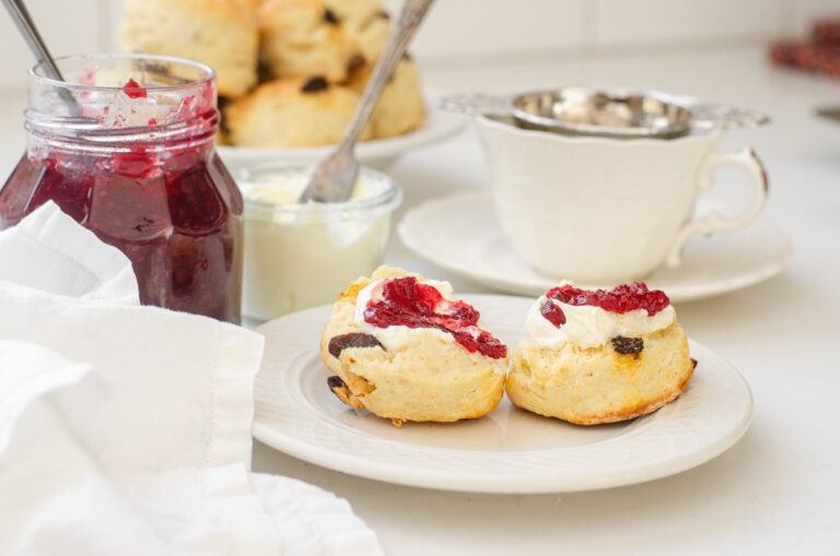 Irish Scones made with buttermilk on a small plate with a teacup, jam, and Devonshire cream in the background.
