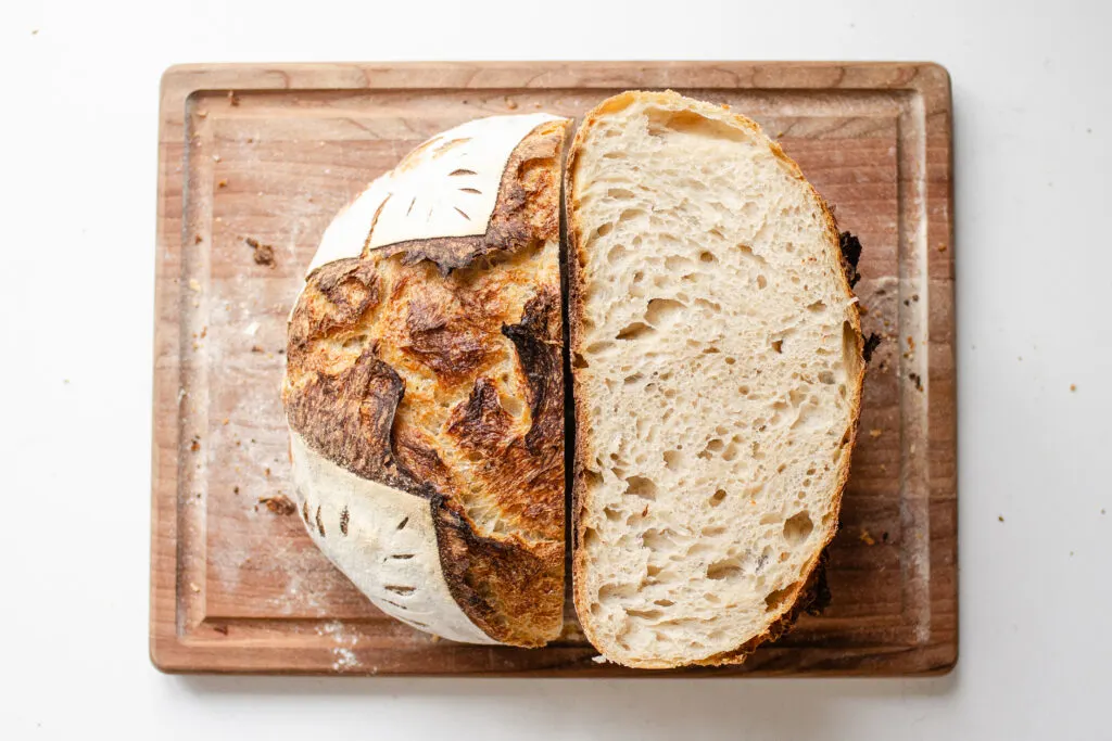 A top down shot of a loaf of sourdough bread that's been baked in a Dutch oven with half upright, and the other half showing the crumb shot.