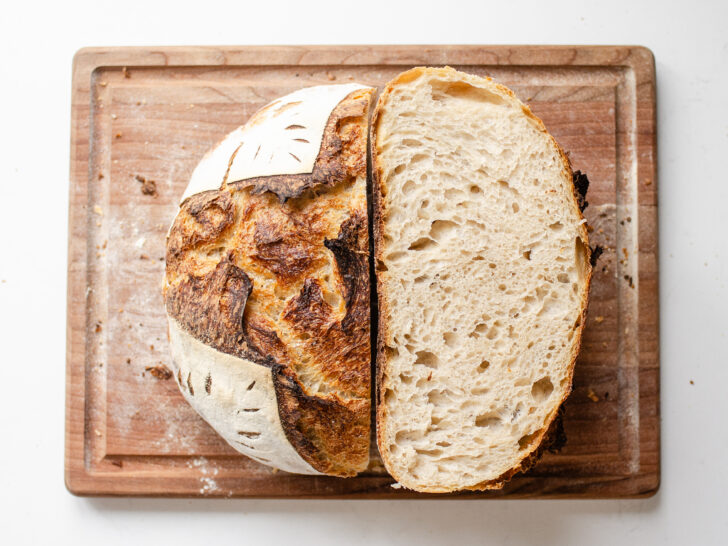 A top down shot of a loaf of sourdough bread that's been baked in a Dutch oven with half upright, and the other half showing the crumb shot.