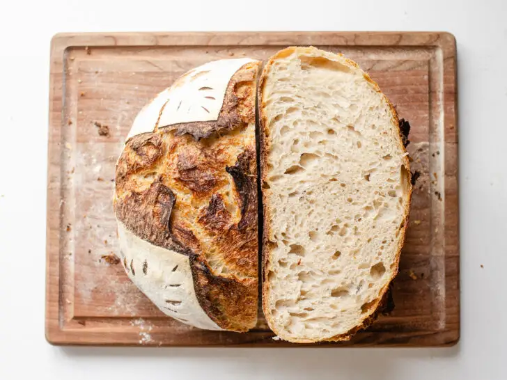 A top down shot of a loaf of sourdough bread that's been baked in a Dutch oven with half upright, and the other half showing the crumb shot.