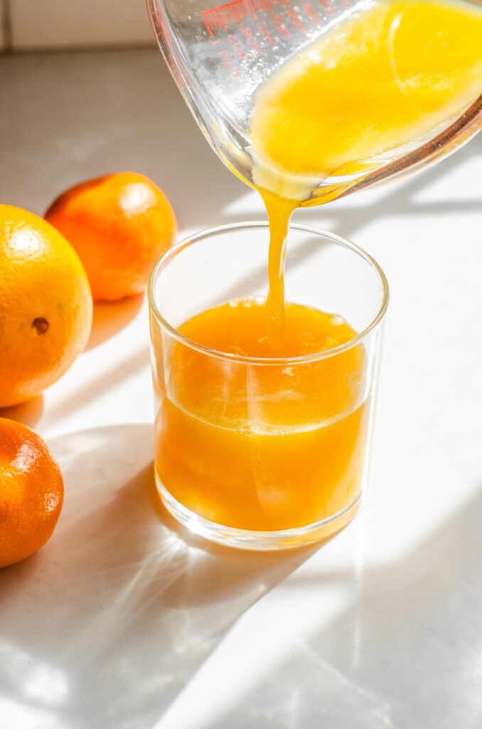 Pouring freshly sqeezed orange juice into a cup on a sunny countertop.