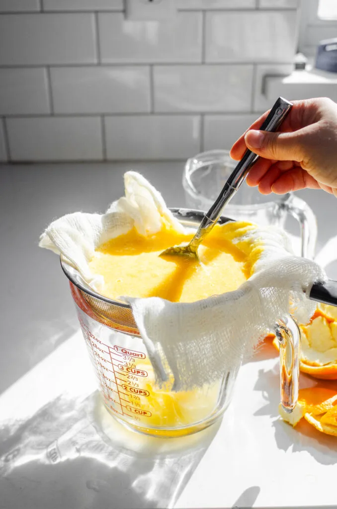 Straining blended orange juice through cheesecloth.
