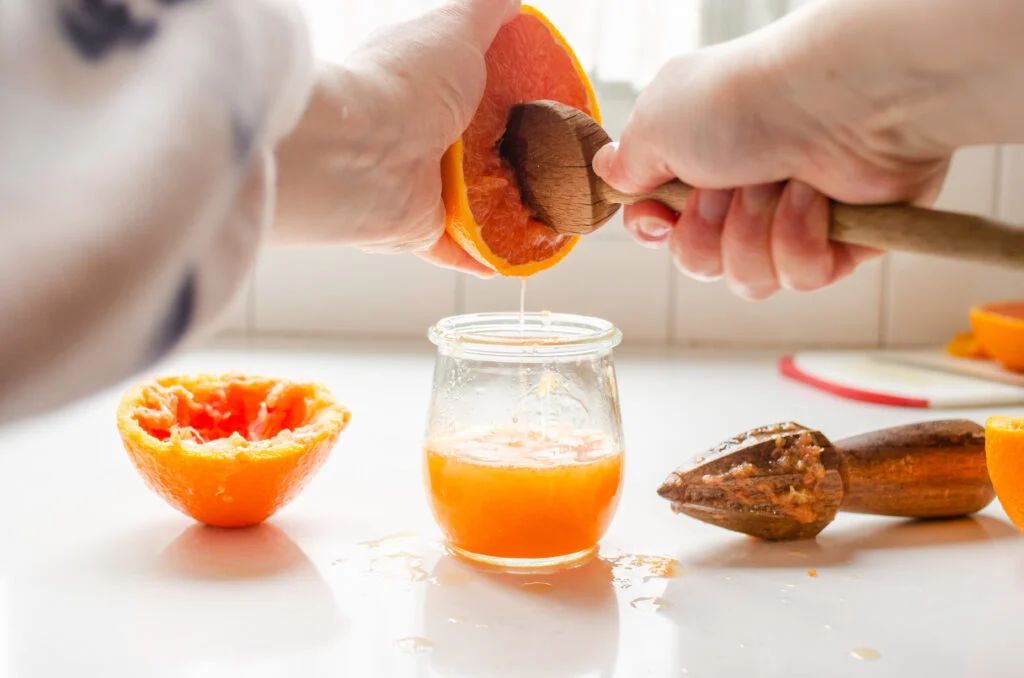 Two hands using a wooden spoon to juice a fresh orange.
