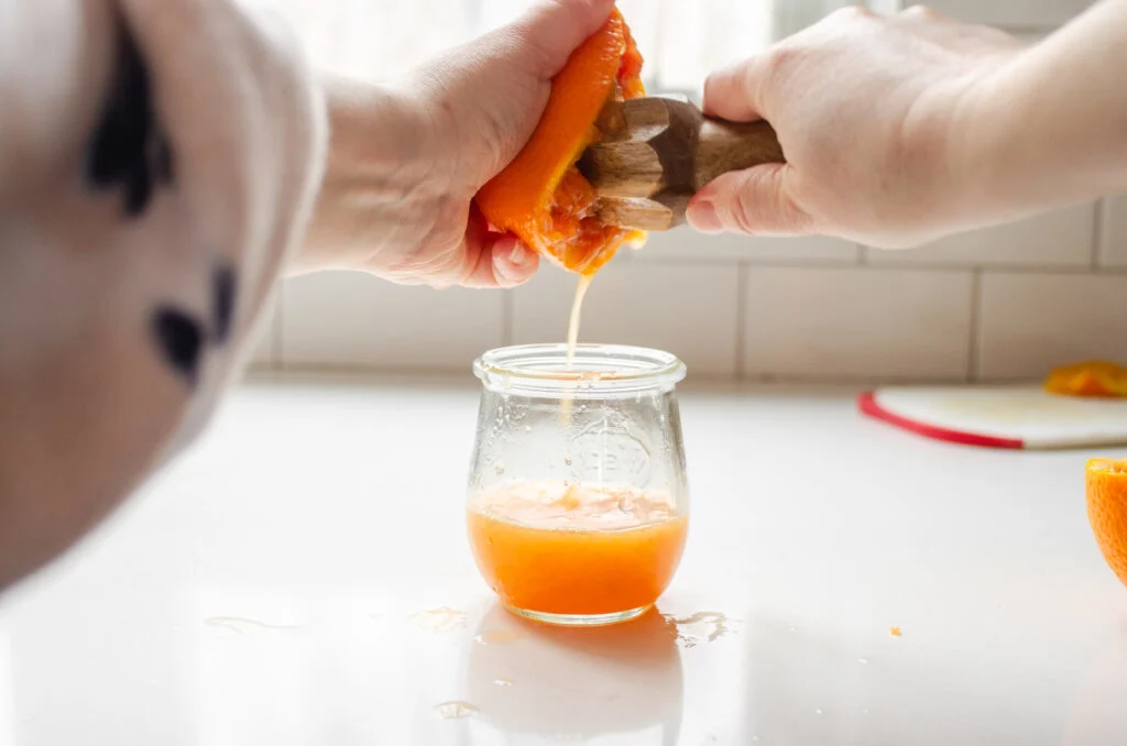 Two hands using a citrus reamer to juice a cara cara orange.