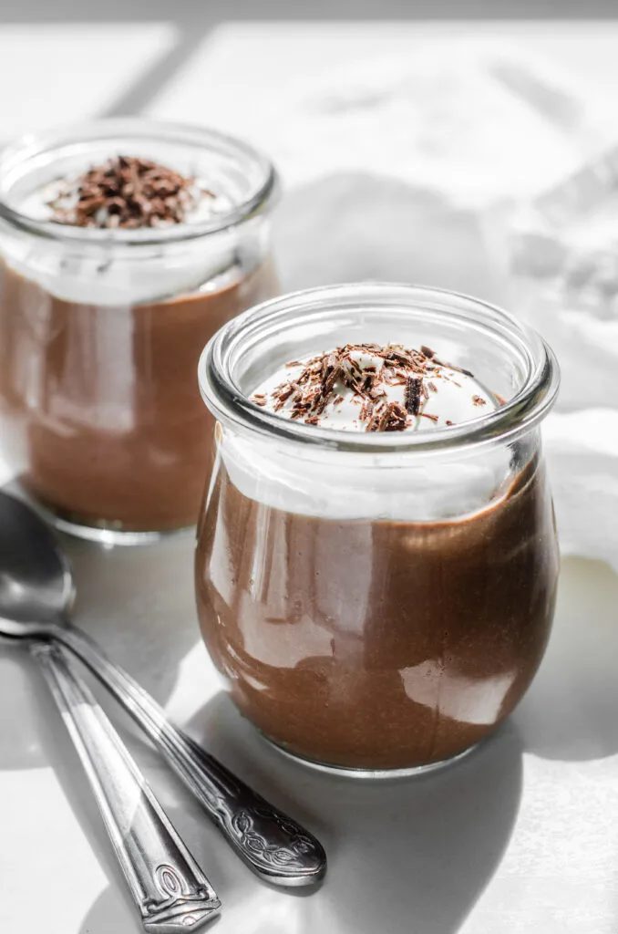 Two Weck mini tulip jars filled with chocolate pudding and topped with whipped cream and chocolate shavings.