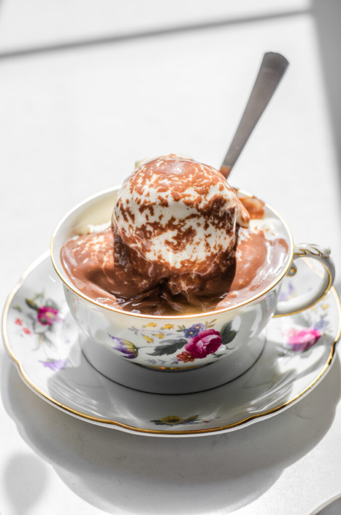 Hot chocolate pudding poured over ice cream in a teacup with a dessert spoon in the ice cream.