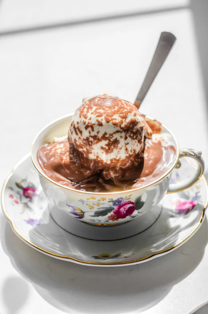Hot chocolate pudding poured over ice cream in a teacup with a dessert spoon in the ice cream.