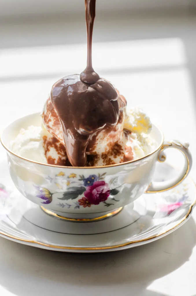 Pouring hot chocolate pudding on top of ice cream in a teacup.