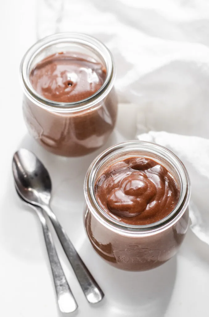 Two Weck jars filled with warm chocolate pudding with two dessert spoons on one side, and a linen napkin on the other.