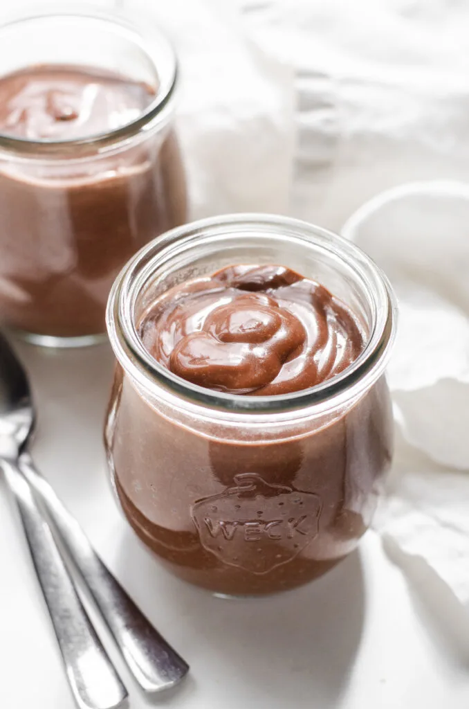 Two Weck jars filled with warm chocolate pudding with two dessert spoons on one side, and a linen napkin on the other.
