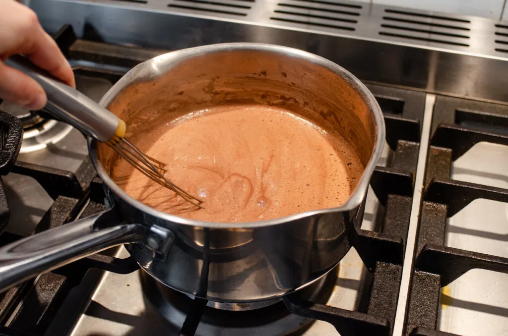 A pot of chocolate pudding cooking over the stove.
